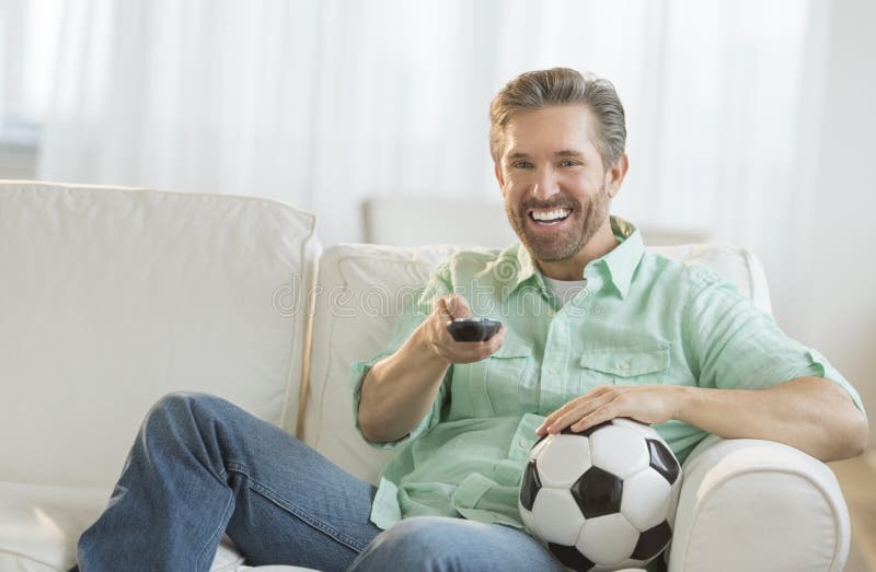 Hombre con el balón de fútbol que ve la TV fotos de archivo Hombre con el balón de fútbol que ve la TV fotos de archivo