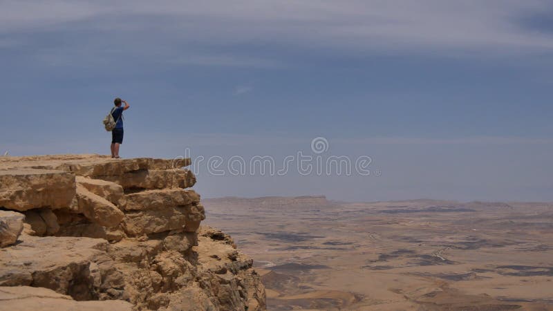Hombre con la mochila que se coloca en el borde del acantilado de la roca de la montaña del desierto