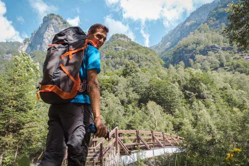 Hombre con la mochila que sonríe a la cámara rodeada por la naturaleza y las montañas asombrosas fotos de archivo libres de regalías Hombre con la mochila que sonríe a la cámara rodeada por la naturaleza y las montañas asombrosas fotos de archivo libres de regalías