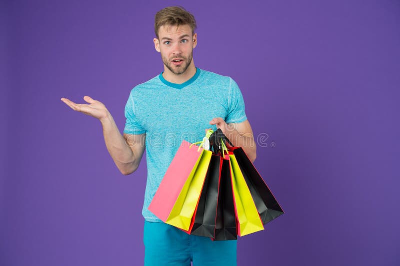 Hombre con los panieres y gesto de mano en el fondo violeta Machista con las bolsas de papel coloridas Comprador de la moda con l imagenes de archivo Hombre con los panieres y gesto de mano en el fondo violeta Machista con las bolsas de papel coloridas Comprador de la moda con l imagenes de archivo