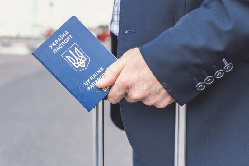 Hombre con traje azul con maleta y pasaporte ucraniano en el aeropuerto. Concepto de viaje de negocios foto de archivo libre de regalías Hombre con traje azul con maleta y pasaporte ucraniano en el aeropuerto. Concepto de viaje de negocios foto de archivo libre de regalías