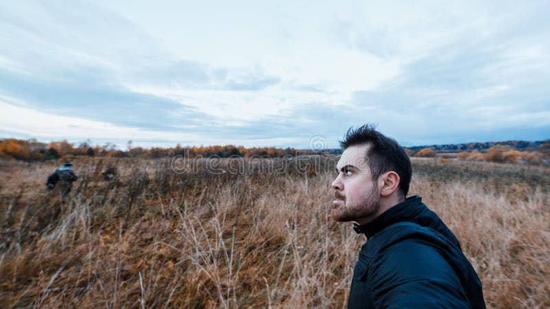Hombre con una expresión maníaca en chaqueta negra que acecha a la víctima en el concepto del bosque del otoño de agravación del fotografía de archivo Hombre con una expresión maníaca en chaqueta negra que acecha a la víctima en el concepto del bosque del otoño de agravación del fotografía de archivo