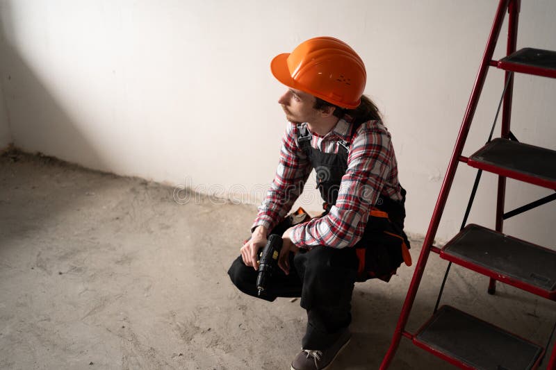 Hombre creador sentado en una sala de renovación con taladro para trabajar imagenes de archivo