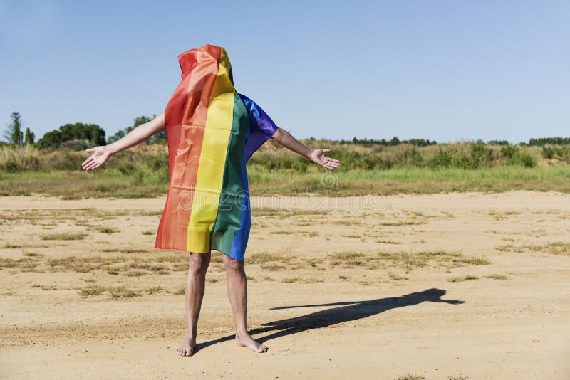 Hombre cubierto con una bandera del arco iris imagen de archivo libre de regalías Hombre cubierto con una bandera del arco iris imagen de archivo libre de regalías