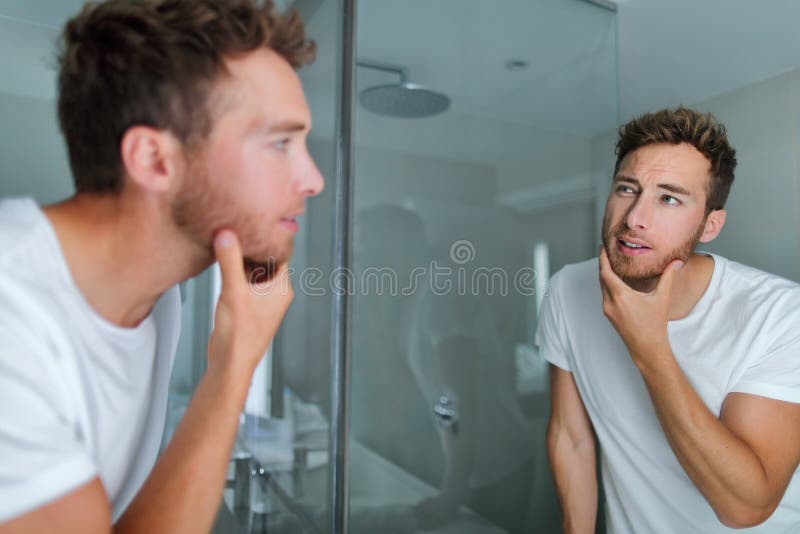Hombre cuidado de la cara mirando en el espejo tocando su barba o salud de la piel. rutina de cuidado de la piel en la mañana de b