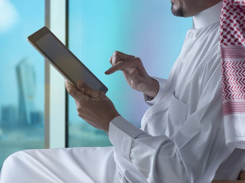 Hombre de Arabia Saudita que usa la tableta al lado de la ventana fotos de archivo Hombre de Arabia Saudita que usa la tableta al lado de la ventana fotos de archivo