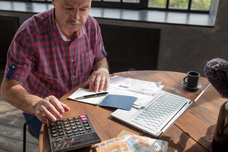 Hombre de la tercera edad ocupado haciendo cálculos, contando dinero y facturas en casa imagen de archivo libre de regalías Hombre de la tercera edad ocupado haciendo cálculos, contando dinero y facturas en casa imagen de archivo libre de regalías