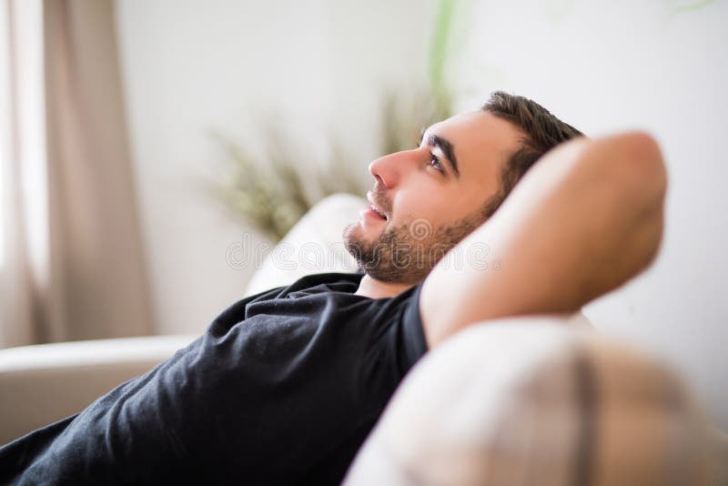 Hombre de la vista lateral que miente y que se relaja en el sofá en casa en la sala de estar fotografía de archivo