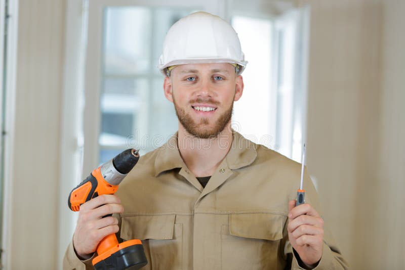 Hombre de mano feliz del constructor trabajando con taladro eléctrico en interiores imagen de archivo