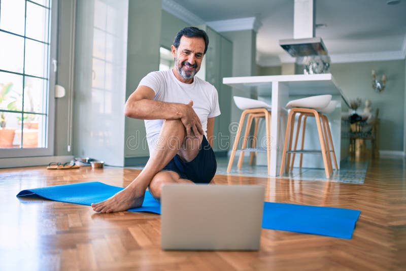 Hombre de mediana edad con barba entrenando y estirando haciendo ejercicio en casa mirando video deportivo en computadora fotografía de archivo libre de regalías