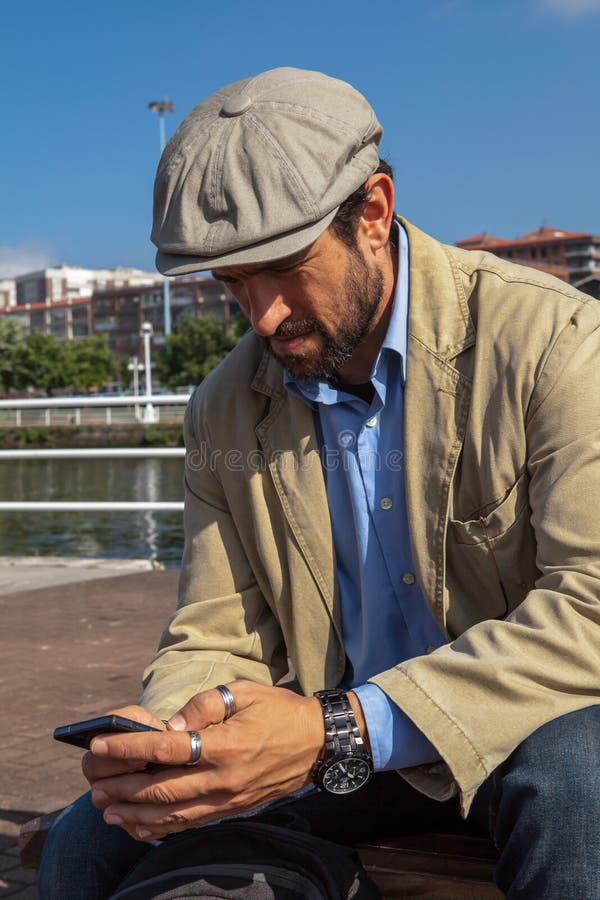 Hombre de mediana edad con la boina irlandesa que mira su smartphone imagen de archivo Hombre de mediana edad con la boina irlandesa que mira su smartphone imagen de archivo