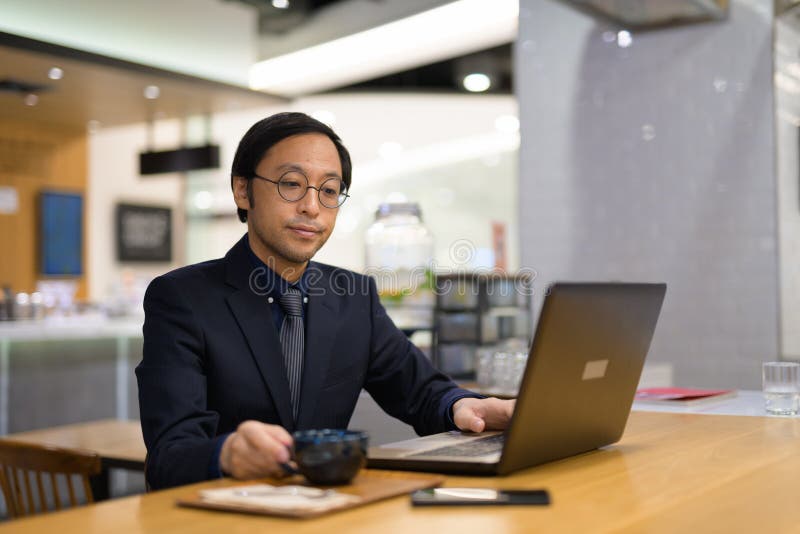 Hombre de negocios asiático que usa el ordenador portátil dentro de la cafetería fotografía de archivo libre de regalías Hombre de negocios asiático que usa el ordenador portátil dentro de la cafetería fotografía de archivo libre de regalías