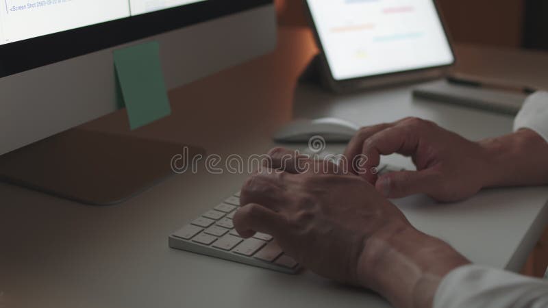 Hombre de negocios asiático tecleando teclado, trabajar tarde usando computadora de escritorio y tablet digital en la oficina del