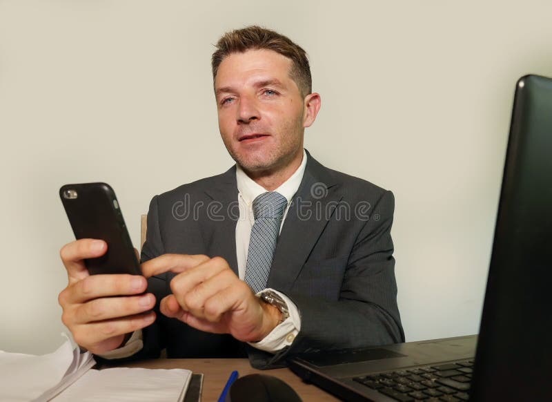 Hombre de negocios atractivo y feliz joven en el funcionamiento del traje y de la corbata en el escritorio del ordenador portátil foto de archivo Hombre de negocios atractivo y feliz joven en el funcionamiento del traje y de la corbata en el escritorio del ordenador portátil foto de archivo