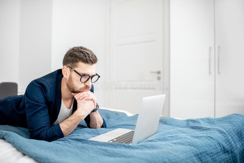 Hombre de negocios con el ordenador portátil en la cama imagenes de archivo Hombre de negocios con el ordenador portátil en la cama imagenes de archivo