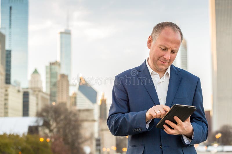 Hombre de negocios con la tableta delante de los edificios de oficinas fotografía de archivo libre de regalías Hombre de negocios con la tableta delante de los edificios de oficinas fotografía de archivo libre de regalías