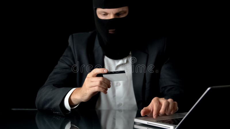 Hombre de negocios en pasamontañas con el dinero de las transferencias de la tarjeta del ordenador portátil y de banco a los asil fotografía de archivo libre de regalías Hombre de negocios en pasamontañas con el dinero de las transferencias de la tarjeta del ordenador portátil y de banco a los asil fotografía de archivo libre de regalías