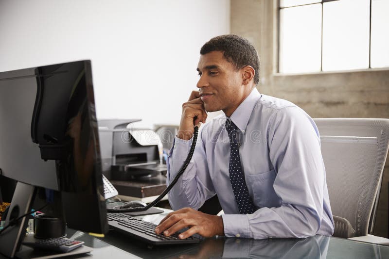 Hombre de negocios en un escritorio de oficina usando el teléfono y el ordenador