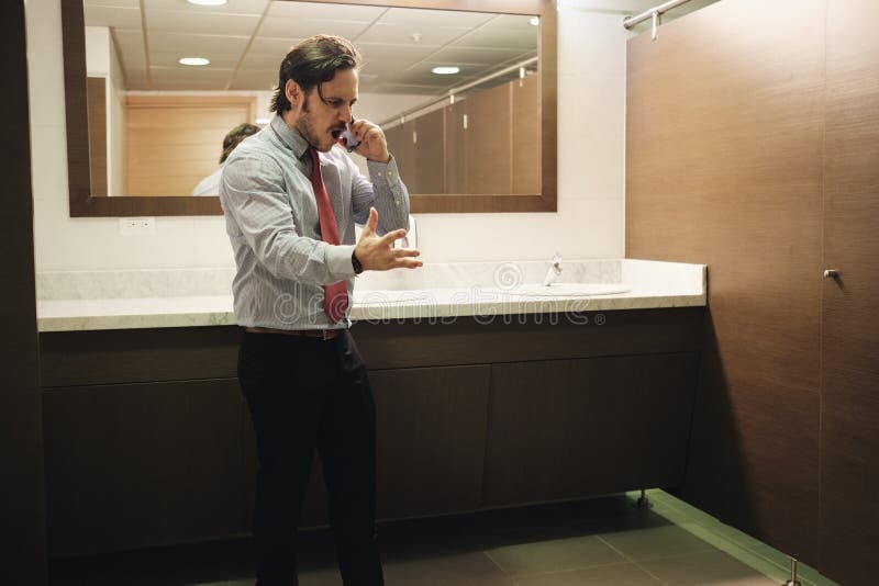 Hombre de negocios furioso que grita en el teléfono celular en lavabo de la oficina imagenes de archivo Hombre de negocios furioso que grita en el teléfono celular en lavabo de la oficina imagenes de archivo