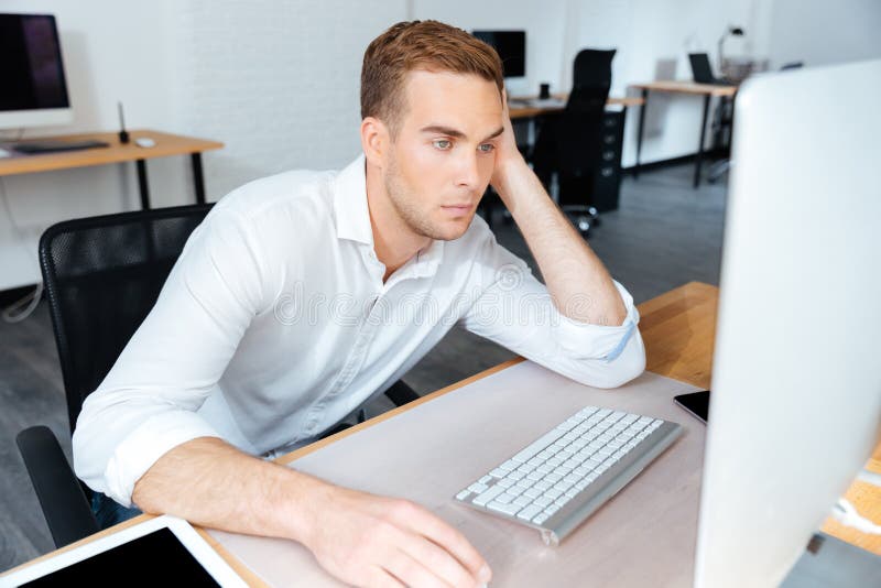Hombre de negocios joven aburrido cansado que trabaja con el ordenador en oficina fotos de archivo libres de regalías Hombre de negocios joven aburrido cansado que trabaja con el ordenador en oficina fotos de archivo libres de regalías