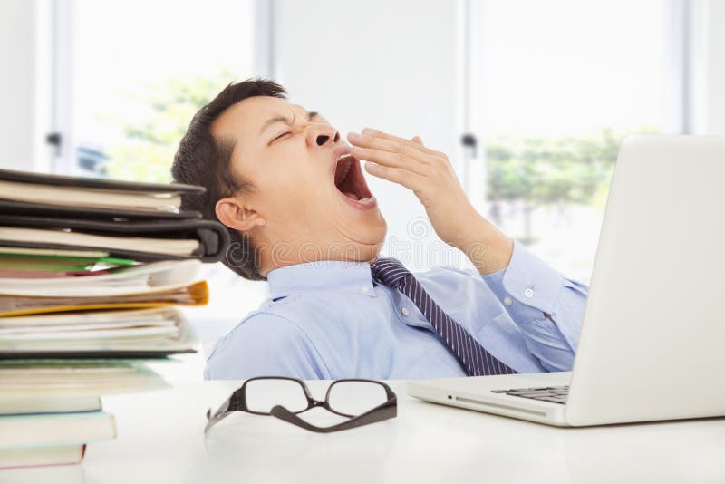 Hombre de negocios joven agotado que bosteza en el trabajo imagenes de archivo Hombre de negocios joven agotado que bosteza en el trabajo imagenes de archivo