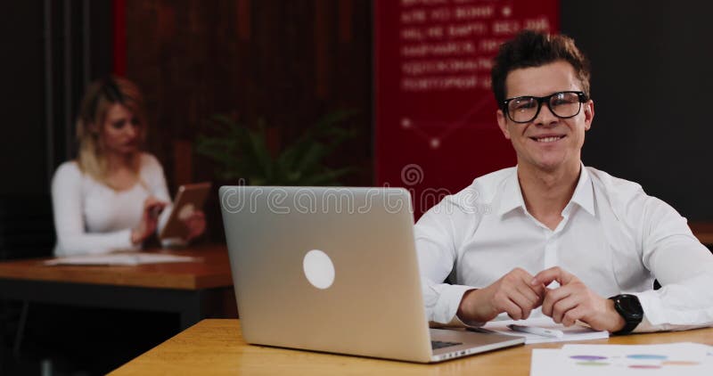 Hombre de negocios joven en vidrios con el ordenador portátil y el papel que trabajan en oficina Negocio, gente, papeleo y