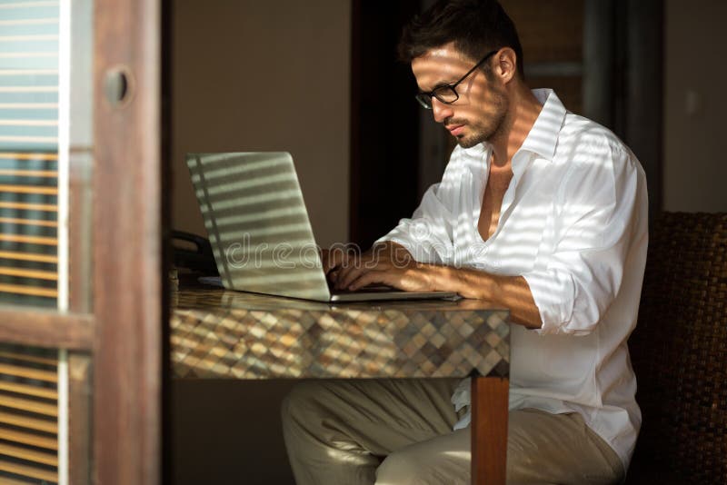 Hombre de negocios joven que se sienta en el escritorio, usando el ordenador portátil foto de archivo Hombre de negocios joven que se sienta en el escritorio, usando el ordenador portátil foto de archivo