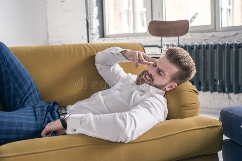 Hombre de negocios preocupante con el dolor de cabeza que miente en el sofá en sala de estar imagen de archivo Hombre de negocios preocupante con el dolor de cabeza que miente en el sofá en sala de estar imagen de archivo