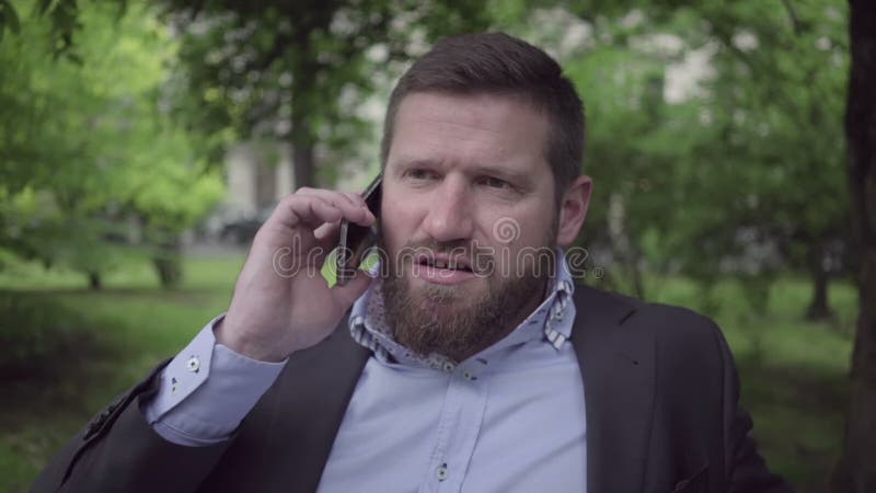 Hombre de negocios que habla por el smartphone, tiro al aire libre, cercano, tiro de la cacerola tiro almacen de metraje de vídeo