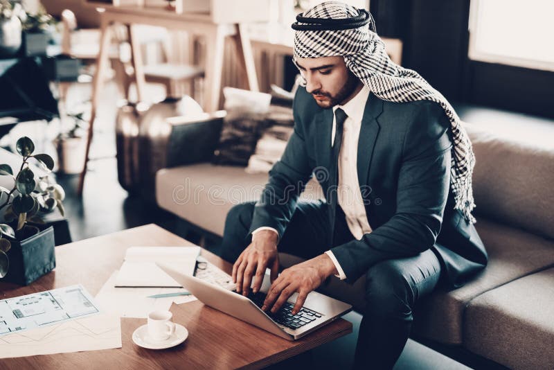 Hombre de negocios que se sienta en el sofá y que mira el ordenador portátil imagen de archivo