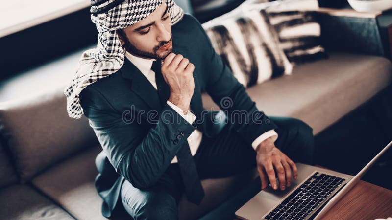 Hombre de negocios que se sienta en el sofá y que mira el ordenador portátil fotografía de archivo