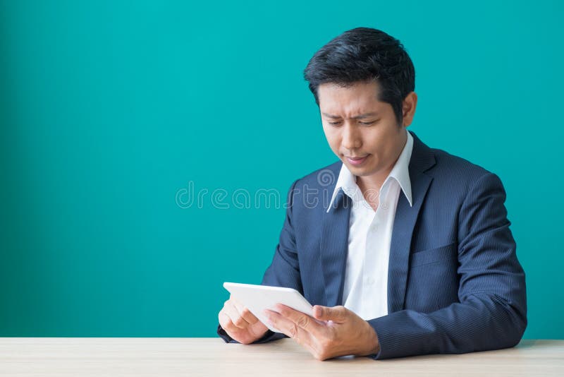Hombre de negocios que se sienta en la tabla de madera y la pared verde y que mira el dow imagen de archivo libre de regalías Hombre de negocios que se sienta en la tabla de madera y la pared verde y que mira el dow imagen de archivo libre de regalías