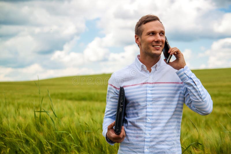 Hombre de negocios que usa el ordenador portátil y el smartphone en campo de trigo fotografía de archivo libre de regalías Hombre de negocios que usa el ordenador portátil y el smartphone en campo de trigo fotografía de archivo libre de regalías