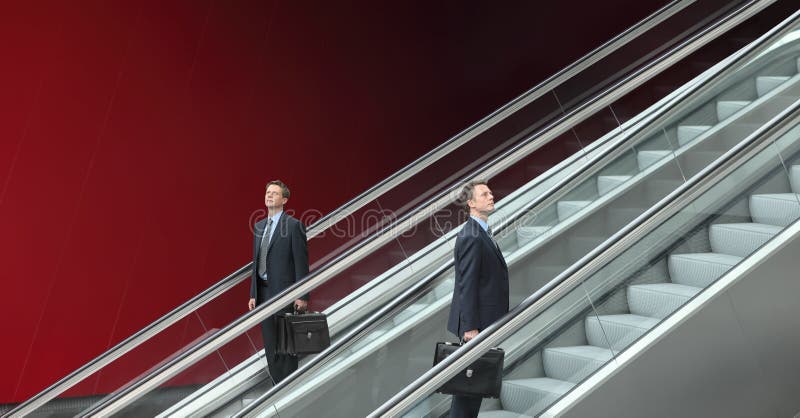 Hombre de negocios que va arriba y abajo de las escaleras móviles, concepto de éxito foto de archivo libre de regalías Hombre de negocios que va arriba y abajo de las escaleras móviles, concepto de éxito foto de archivo libre de regalías