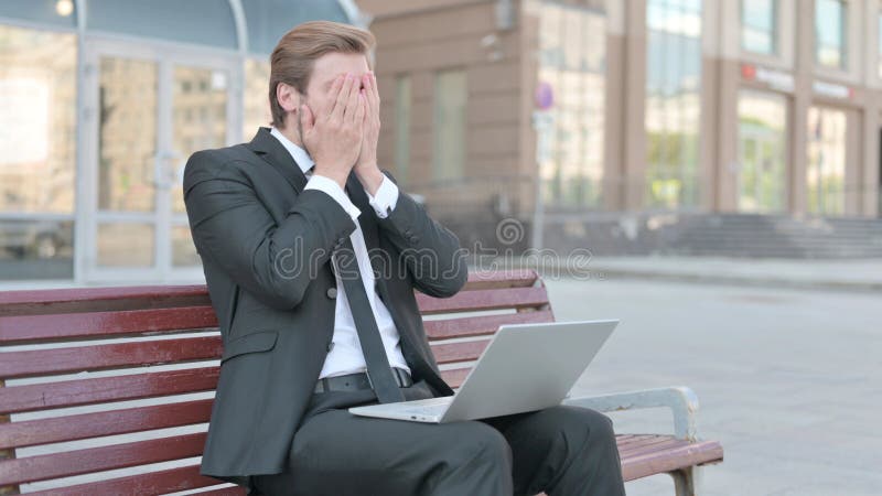 Hombre de negocios reaccionando a la pérdida en el portátil mientras se sienta al aire libre en el banco imagen de archivo libre de regalías