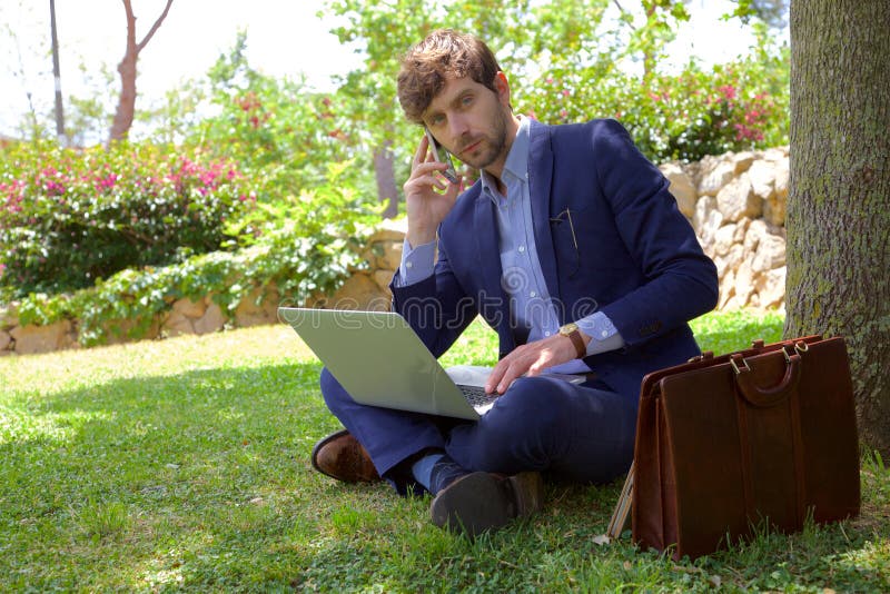 Hombre de negocios serio en el teléfono mientras que trabaja con PC en parque fotos de archivo libres de regalías Hombre de negocios serio en el teléfono mientras que trabaja con PC en parque fotos de archivo libres de regalías