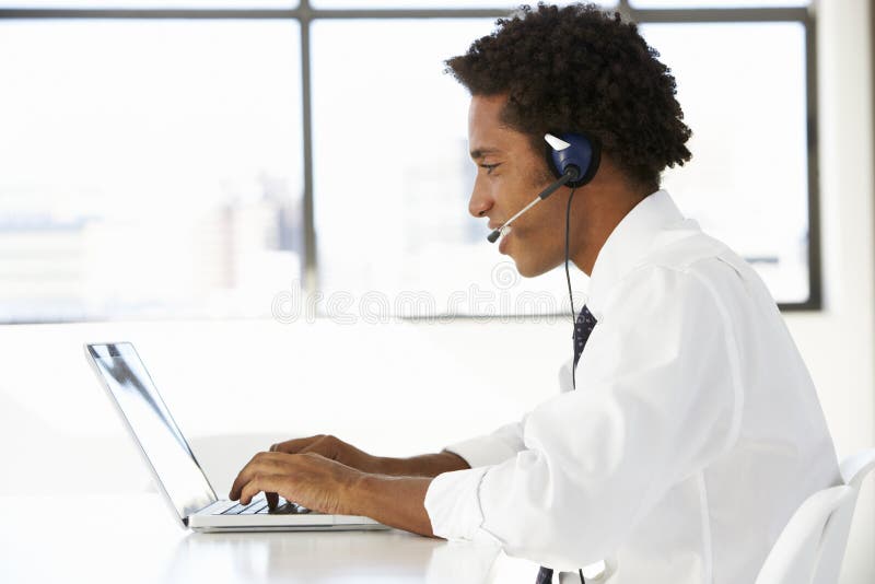 Hombre de negocios Sitting At Desk en oficina usando las auriculares que llevan del ordenador portátil