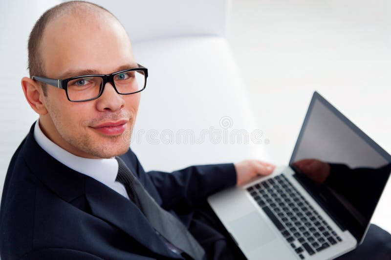 Hombre de negocios sonriente joven que se sienta con el ordenador portátil fotos de archivo libres de regalías Hombre de negocios sonriente joven que se sienta con el ordenador portátil fotos de archivo libres de regalías