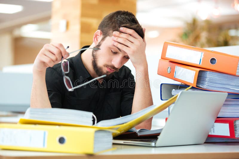 Hombre de negocios triste que se sienta en la tabla con muchas carpetas imagenes de archivo Hombre de negocios triste que se sienta en la tabla con muchas carpetas imagenes de archivo