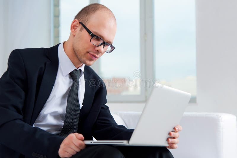 Hombre de negocios usando el ordenador portátil en el sofá fotos de archivo libres de regalías Hombre de negocios usando el ordenador portátil en el sofá fotos de archivo libres de regalías