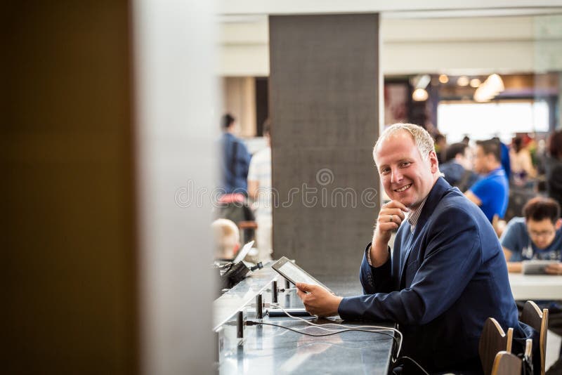 Hombre de negocios usando su tableta en el aeropuerto imágenes de archivo libres de regalías Hombre de negocios usando su tableta en el aeropuerto imágenes de archivo libres de regalías