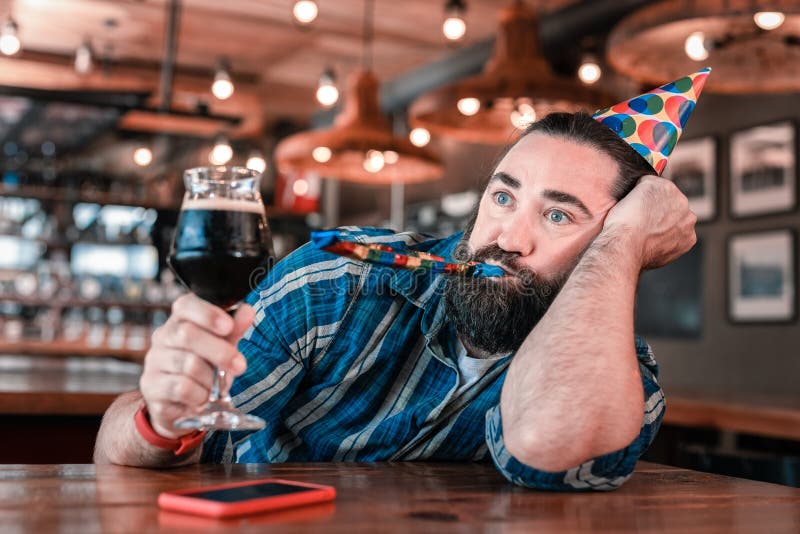 Hombre de ojos azules que sostiene el vidrio de cerveza oscura mientras que asiste a cumpleaños foto de archivo Hombre de ojos azules que sostiene el vidrio de cerveza oscura mientras que asiste a cumpleaños foto de archivo