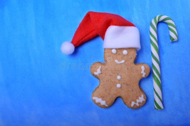 Hombre de pan de jengibre que lleva un sombrero rojo y blanco con un bastón de caramelo verde contra el fondo azul fotografía de archivo libre de regalías Hombre de pan de jengibre que lleva un sombrero rojo y blanco con un bastón de caramelo verde contra el fondo azul fotografía de archivo libre de regalías