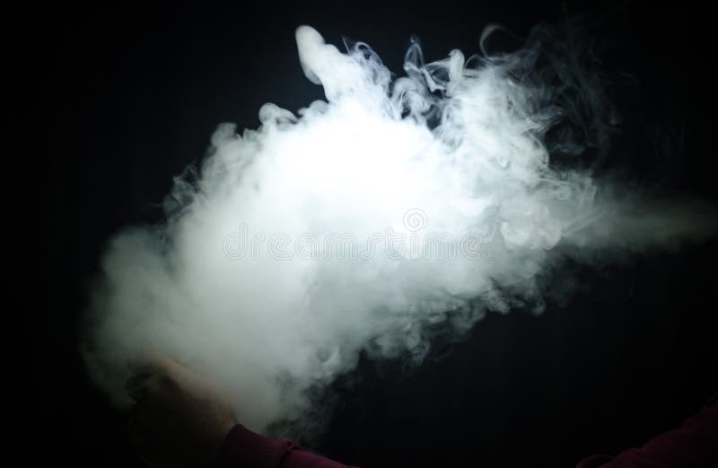 Hombre de Vaping que lleva a cabo una MOD Una nube del vapor Fondo negro Vaping un cigarrillo electrónico con mucho humo