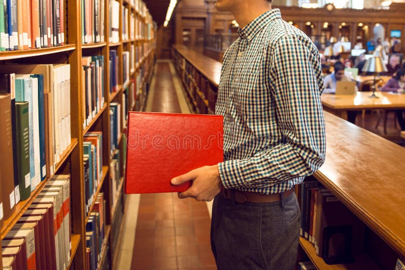 Hombre del estudiante que toma el libro del estante en biblioteca pública y que va a leer fotos de archivo libres de regalías Hombre del estudiante que toma el libro del estante en biblioteca pública y que va a leer fotos de archivo libres de regalías