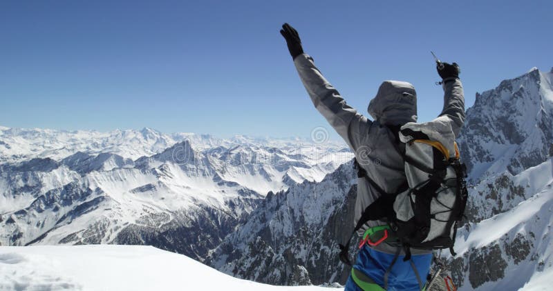 Hombre del montañés del escalador que alcanza el top nevoso del soporte con el hacha de hielo en día soleado Actividad del esquí