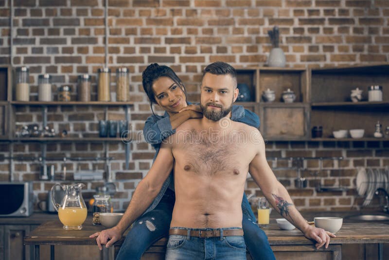 Hombre descamisado barbudo y su novia que abrazan en cocina fotos de archivo Hombre descamisado barbudo y su novia que abrazan en cocina fotos de archivo