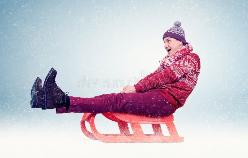 Hombre divertido en suéter y casquillo rojos en el trineo en la nieve, diversión del invierno del concepto imagenes de archivo