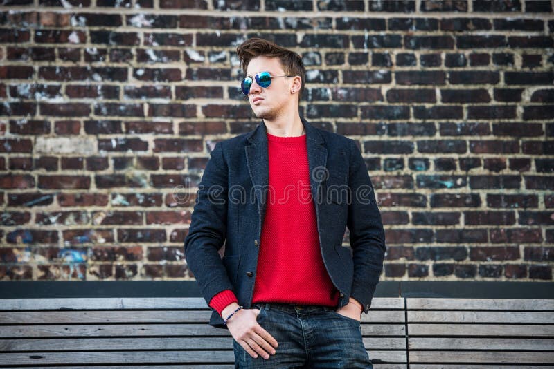 Hombre elegante adulto joven de moda que presenta el pulower rojo al aire libre que lleva, vaqueros, la chaqueta del algodón y la foto de archivo libre de regalías Hombre elegante adulto joven de moda que presenta el pulower rojo al aire libre que lleva, vaqueros, la chaqueta del algodón y la foto de archivo libre de regalías