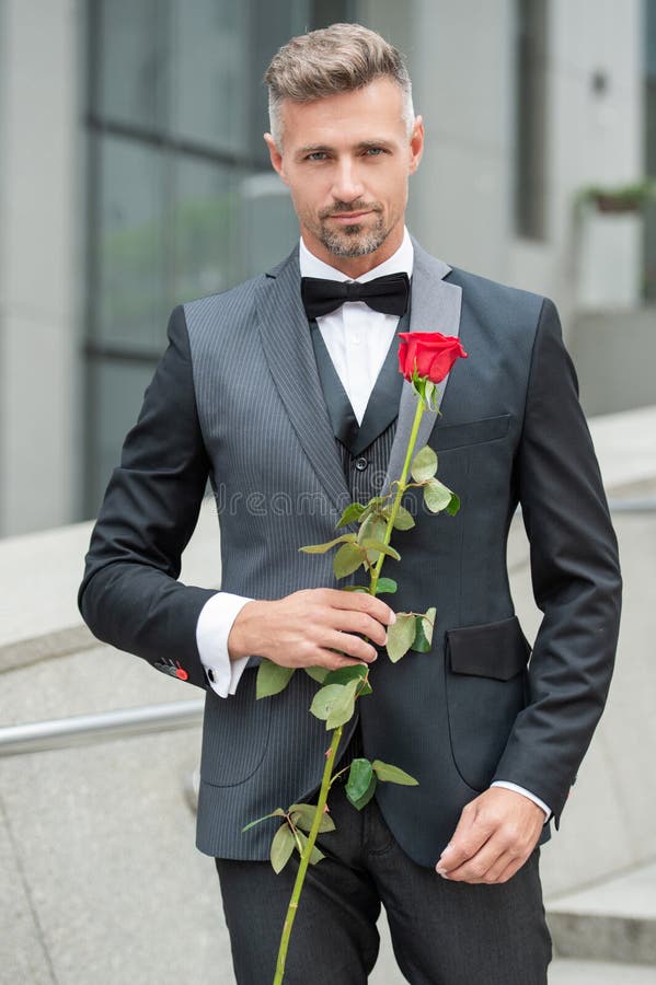 Hombre elegante con esmoquin negro. hombre con el tazón de esmoquín al aire libre. guapo hombre de esmoquin con rosa rojo fotografía de archivo libre de regalías